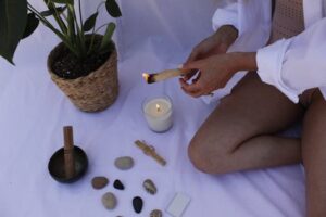 A serene meditation setup with candle, palo santo, stones, and potted plant on a white blanket.